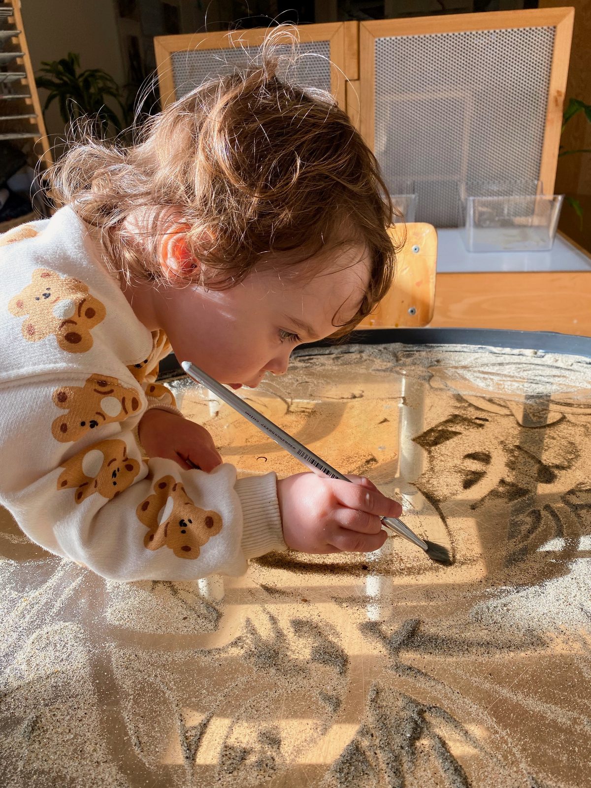 A child painting in sand at the light table, absorbed in a moment of discovery